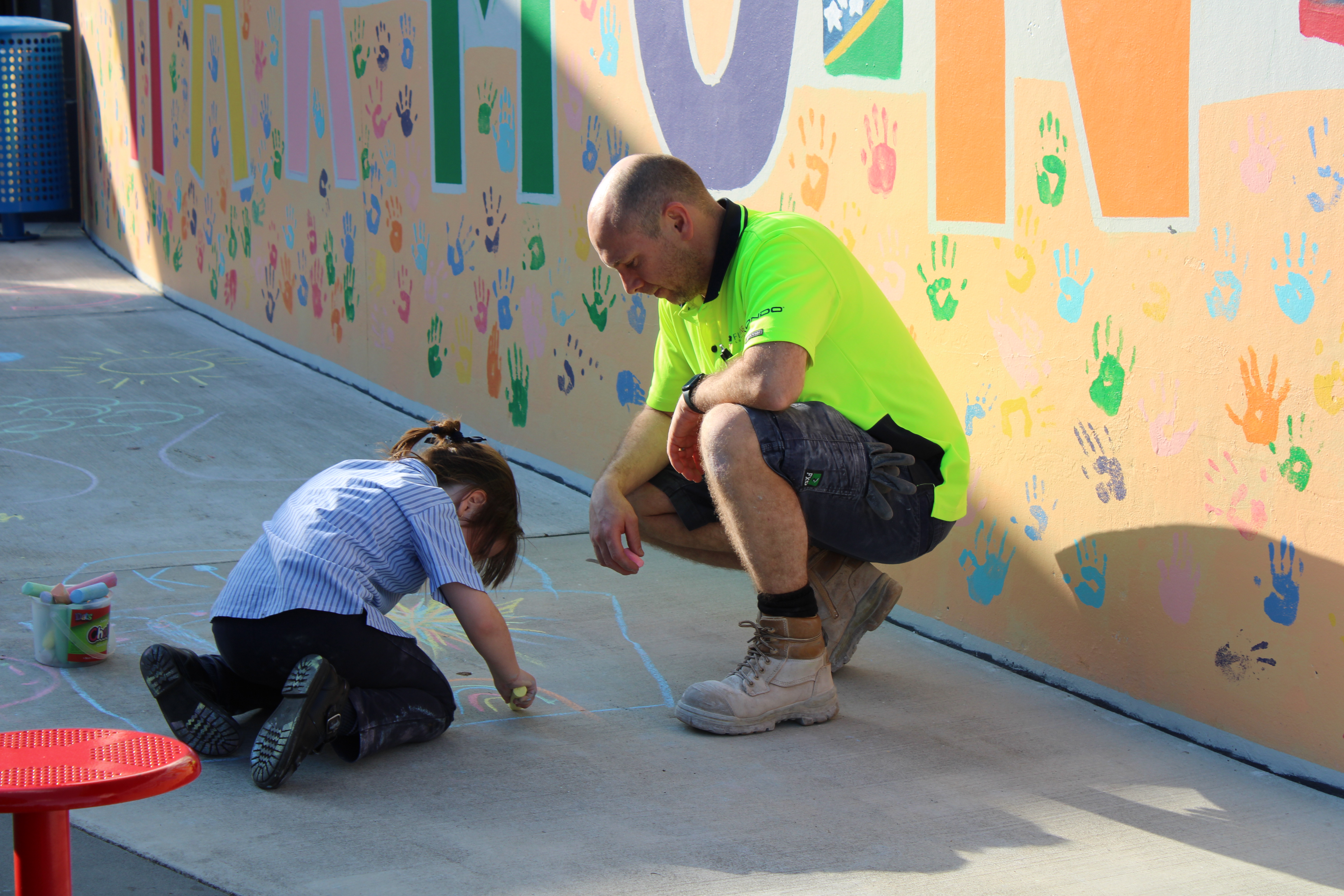 Student drawing with chalk alongside an adult in an outdoor learning space, showing creativity, collaboration and active play