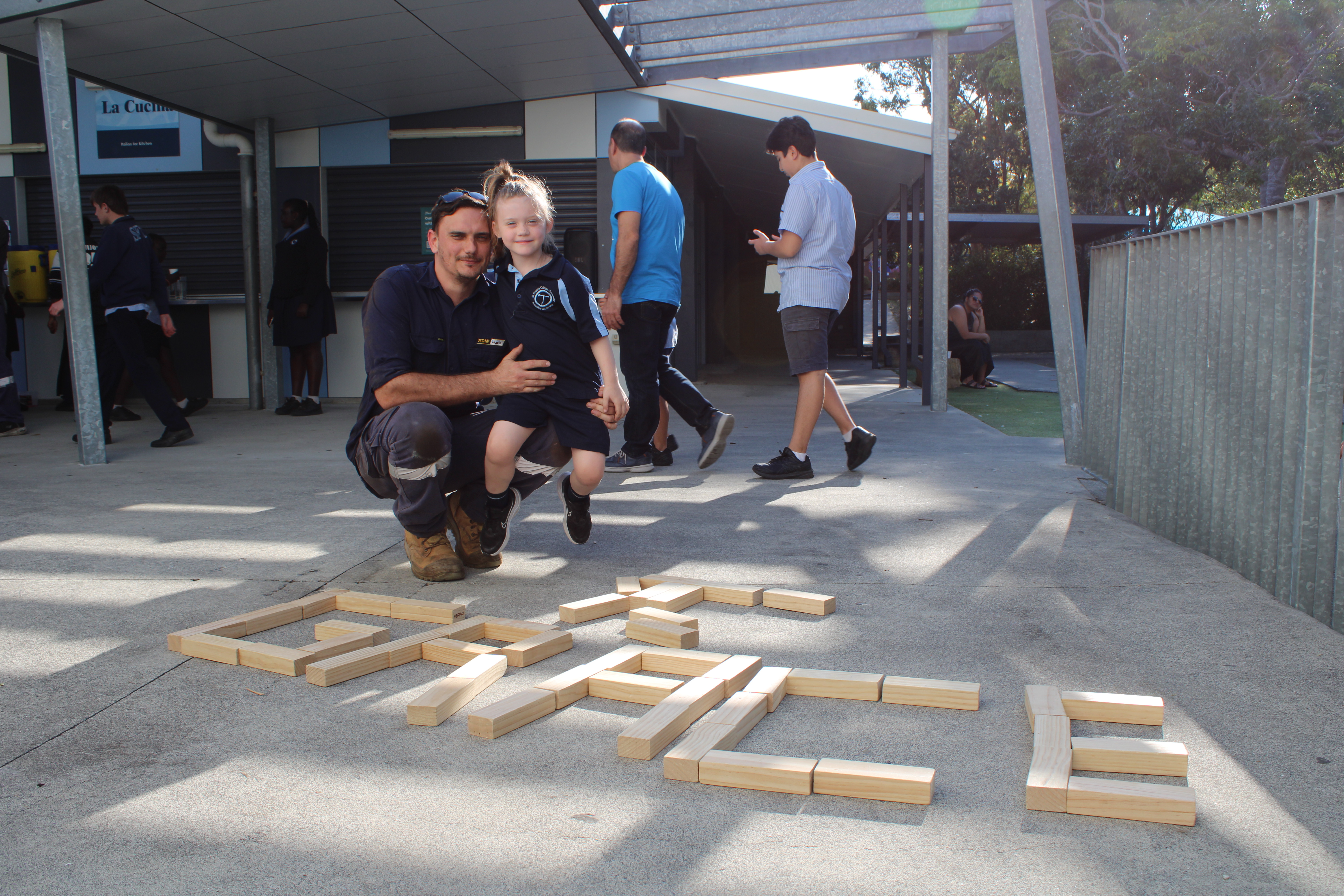 Student and adult working together to build with wooden blocks in a school playground, highlighting hands-on learning and community connection