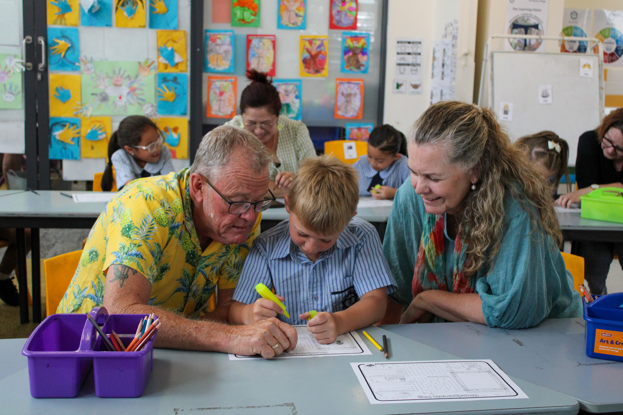 Student receiving guidance from adults while completing classroom work, demonstrating supportive learning partnerships and engagement in literacy activities