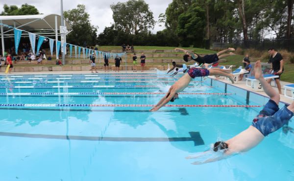 Students diving into swimming lanes during a school event, highlighting participation and water safety skills