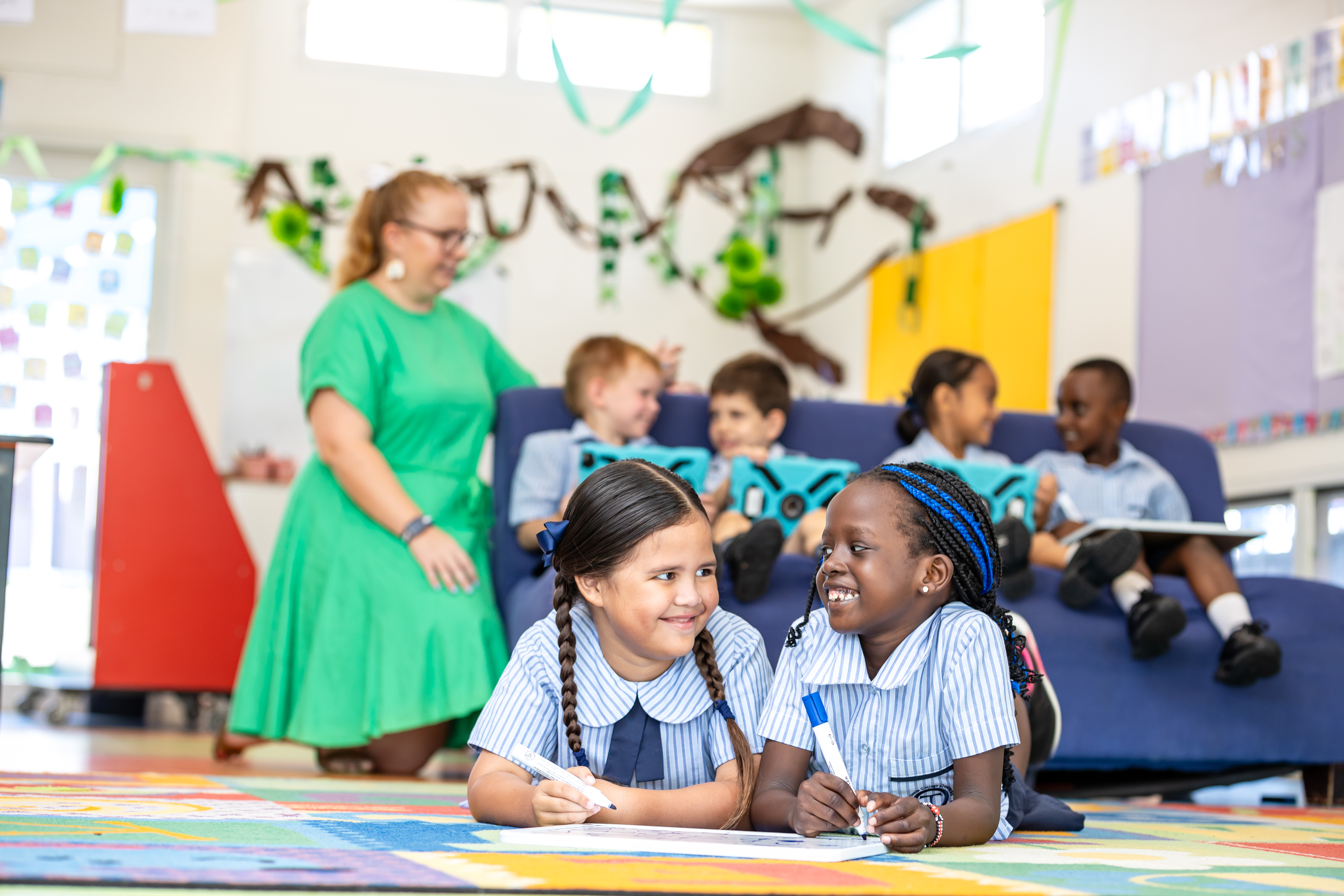 Early years students learning together on the floor with teacher support, promoting collaboration, engagement and foundational literacy development