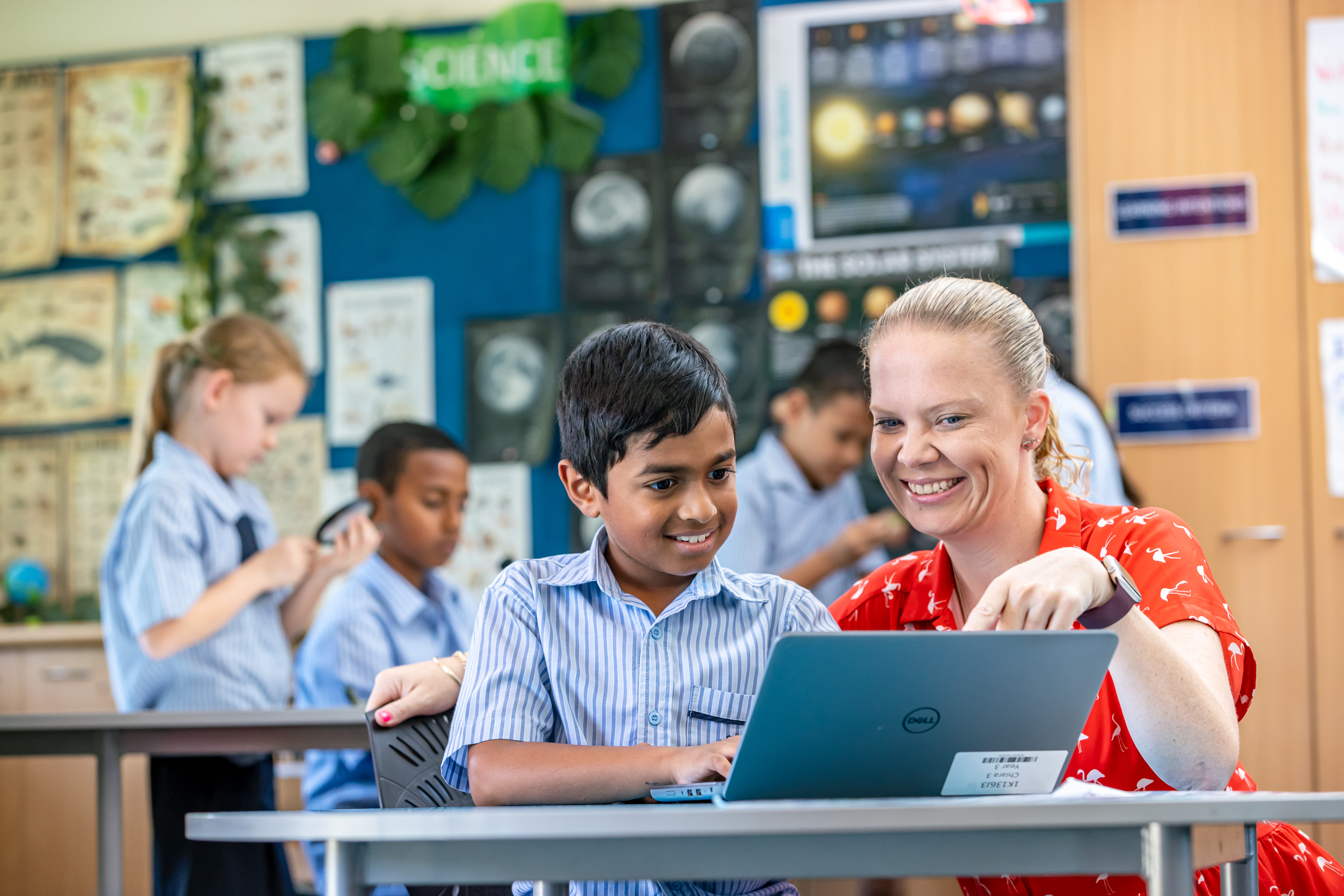 Teacher supporting a student using a laptop during a science lesson, promoting guided learning, digital skills and student engagement