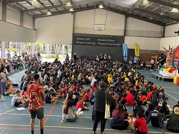 Whole school gathered for assembly in a multipurpose hall focused on community values and participation